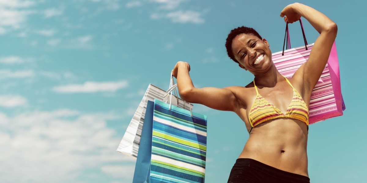 A happy woman in a bikini holds  several gift bags aloft against a blue sky background.
