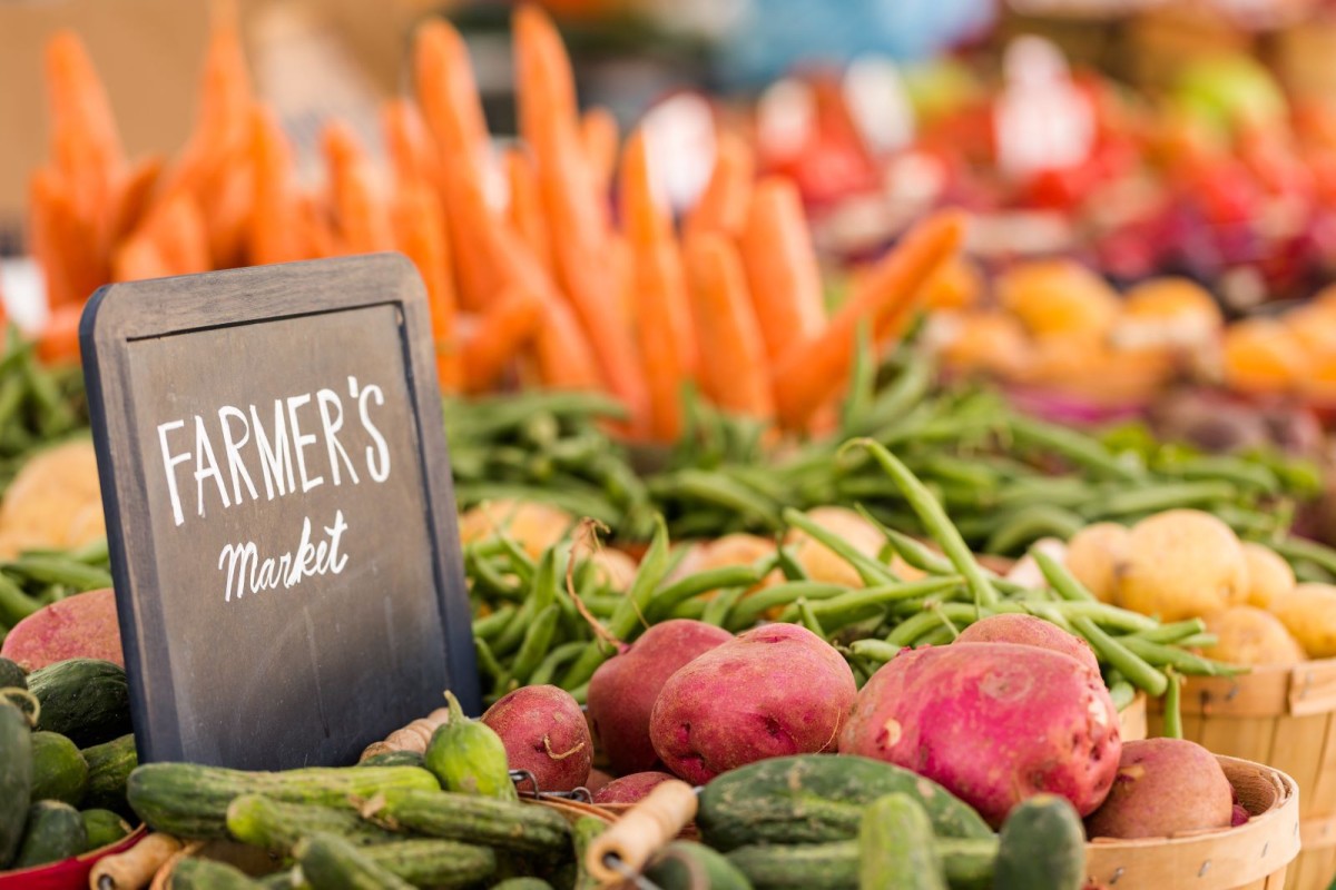 A variety of vegetables are in large baskets with a small sign that reads "Farmer's Market."